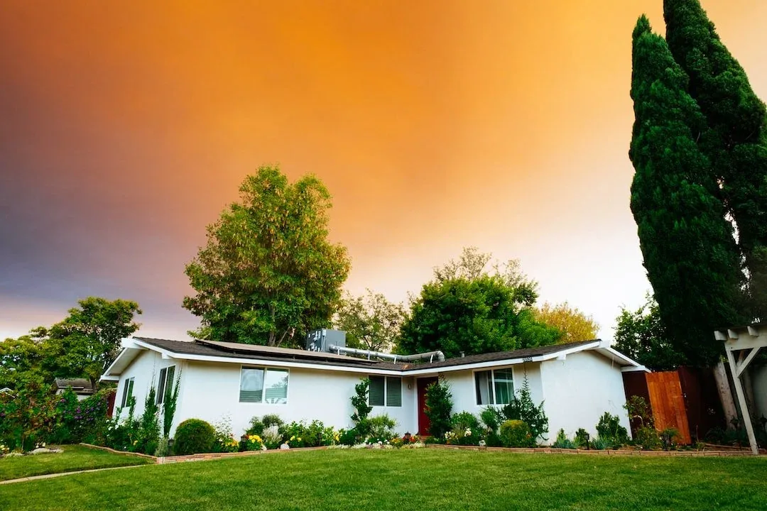 A single-story ranch home with a green lawn and mature trees under a warm evening sky