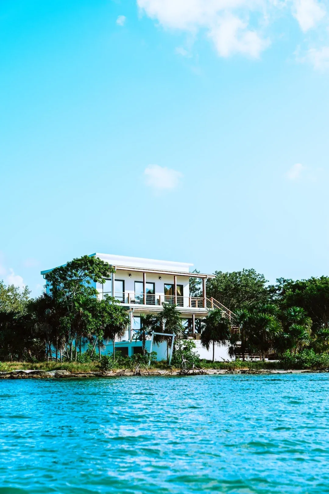 A modern waterfront home with a wide upper deck, framed by palms